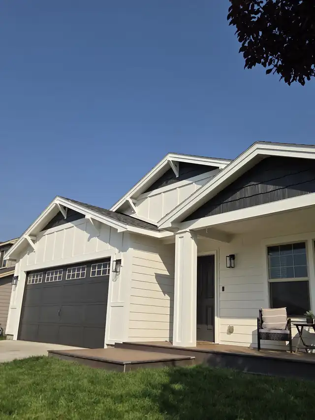 White craftsman house with charcoal gable trim and a charcoal garage door under a blue sky
