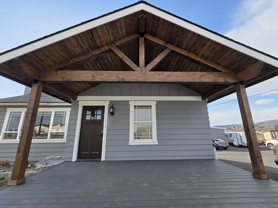 Grey cottage with white window trim, board and batten gable and a dark entry door under a timber porch, painted by PNW Paint Company