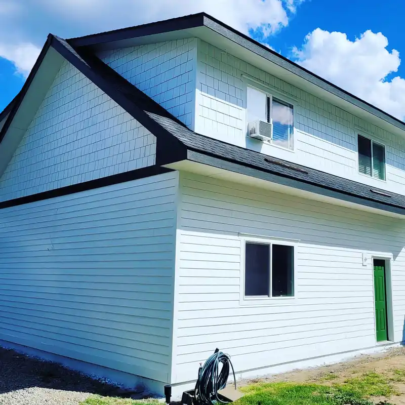 Two-storey house in white lap siding with black trim and a green door, freshly painted