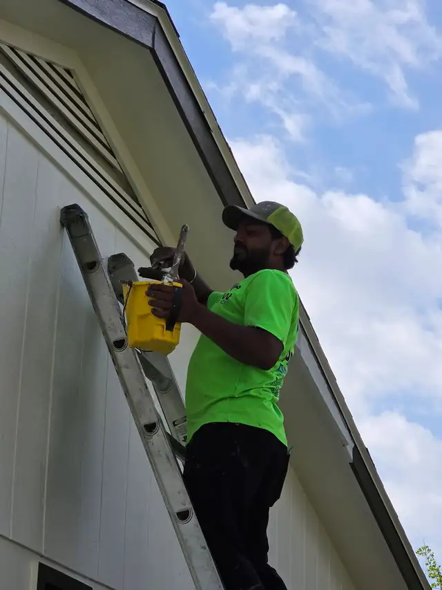 A painter on a ladder scraping and prepping a gable