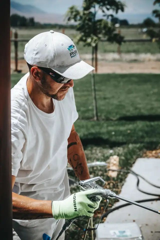 A painter in a PNW cap holding an airless paint sprayer